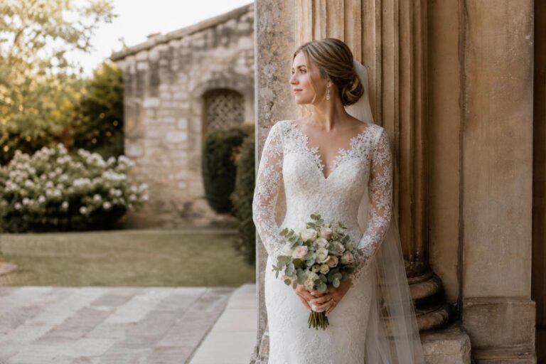 Bride in a lace wedding dress with sleeves, long sheer lace arms and elegant A-line skirt in soft natural light