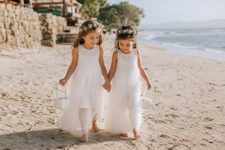 Beach flower girl dresses in ivory lace and chiffon on a sandy shoreline, airy and romantic for a coastal wedding