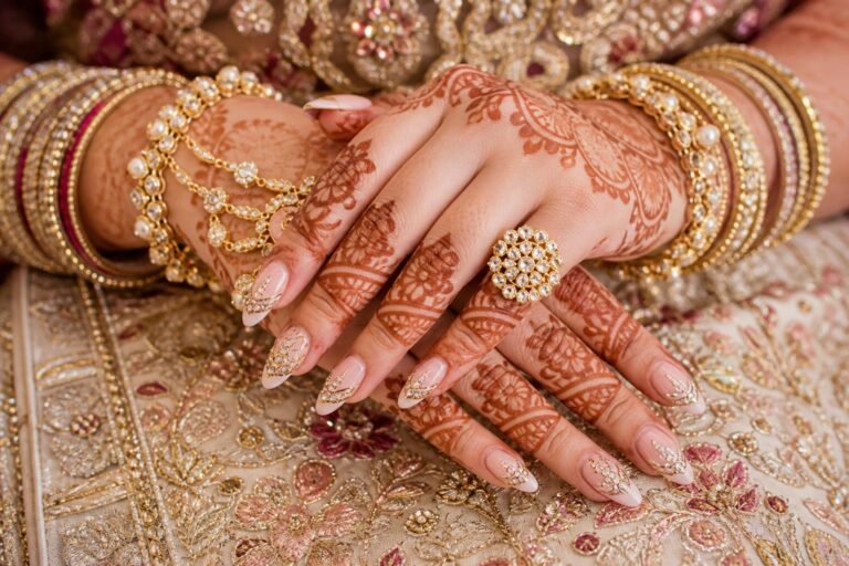Indian wedding nails with glossy red polish, gold foil accents, and delicate crystals in a close-up bridal hand shot