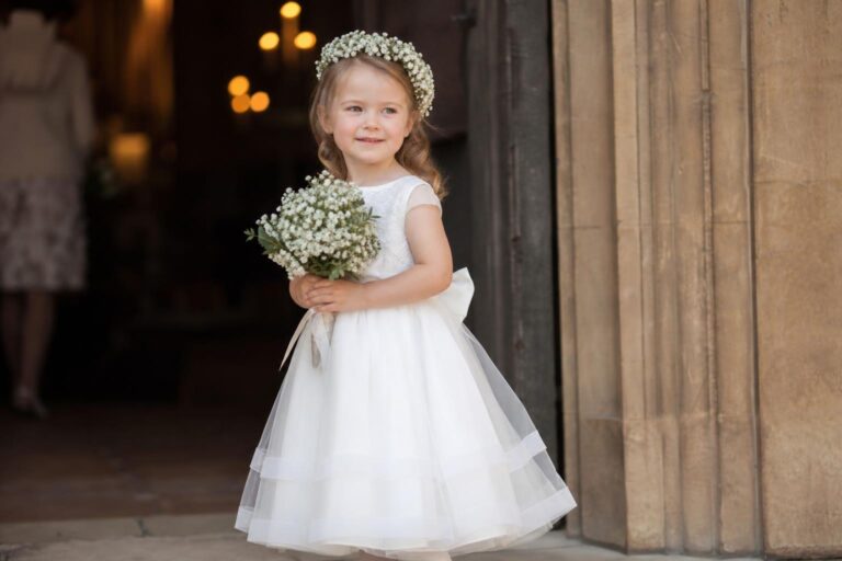 White flower girl dresses in satin with puff sleeves and a pleated knee-length skirt, styled for a timeless wedding aisle
