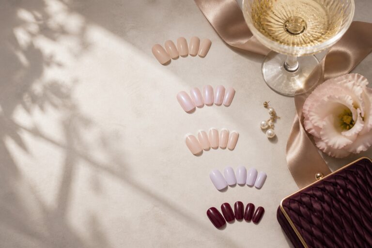Wedding guest nails capsule colors arranged beside champagne, silk, pearls, flowers, and a velvet clutch